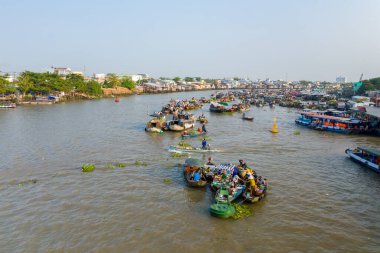 Gündüz vakti nehir manzarası, Güney Vietnam 'daki Can Tho, Mekong Deltası' ndaki Cai Rang yüzer pazarında canlı bir pazar teknesi geçit törenini gösteriyor. Görüntü nehir kenarındaki evler ve renkli gemi kümeleriyle dolu hareketli bir su yoluna sahip.