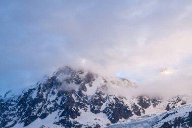 Alacakaranlıkta Aiguille du Midi 'nin engebeli, karla kaplı yamaçlarında yumuşak bulutlar sürükleniyor, Fransız Alpleri' nde sakin ve atmosferik bir alp manzarası yaratıyor..