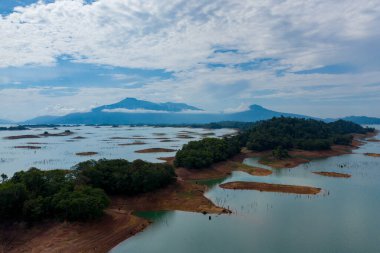 Laos 'taki Nam Ngum Rezervuarı' nın sakin mavi sularından sayısız küçük adalar ve yemyeşil tepeler doğar. Uzak dağlar ve katmanlı bulutlarla dolu dramatik bir gökyüzü ölçek ve doğal sükunet hissi yaratır..