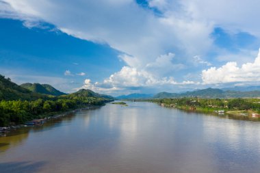 Luang Prabang, Laos yakınlarındaki yemyeşil tepeler arasında akan Mekong Nehri 'nin geniş manzarası. Dramatik kümülüs bulutları durgun su ve orman manzarasının üstündeki mavi gökyüzünü dolduruyor..