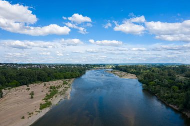 Loire Nehri 'nin kumlu kıyılar ve yoğun yeşil ormanlar arasındaki kıvrımlı görüntüsü dağınık kümülüs bulutlarıyla kaplı bir gökyüzünün altında. Sakin yaz manzarası ufuktaki uzak bir köye doğru uzanıyor..