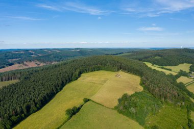 Morvan tepelerinde sık çam ağaçlarıyla çevrili yeşil çayırların havadan görünüşü. Yaz manzarası açık ve sakin. Parlak mavi gökyüzünün altında dağınık bulutlar var..