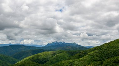 Geniş yemyeşil tepeler Phou Khoun ve Luang Prabang, Laos kırsalındaki kalın ve dokulu bulutlarla dolu dramatik bir gökyüzünün altındaki uzak sisli tepelere doğru genişliyor. Manzara doğal desenleri ve canlılığı yakalar.