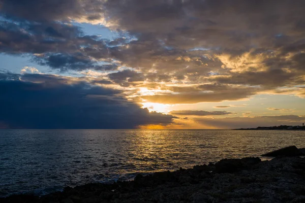 Altın güneş ışığı Adriyatik Denizi üzerindeki dramatik bulutları yararak dalgalı su ve kayalık kıyı şeridinde canlı yansımalar oluşturdu. Sahne, aydınlık gökyüzü ve karanlık kıyı siluetinin alacakaranlıktaki kontrastını yakalıyor..