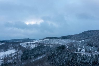 Morvan bölgesinde yoğun çam ormanları ve yuvarlanan tepelerden oluşan kışın manzarası karla kaplandı. Dolambaçlı bir yol, bulutlu mavi gökyüzünün altındaki buzlu ormanlık alandan geçer ve huzurlu ve uzak bir kış manzarası yaratır..