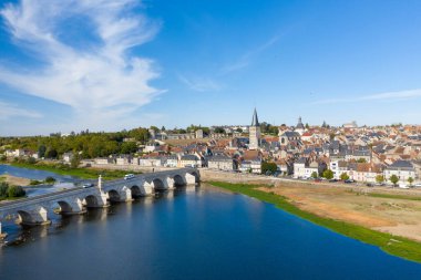 Loire Nehri 'ni geçen taş köprüsü, geleneksel çatıları ve berrak mavi gökyüzünün altındaki önemli kilise kulesiyle La Charite sur Loire' ın yüksek manzarası. Manzaralı kasaba manzarası, ortaçağ mimarisiyle, merkezdeki yemyeşil nehir kenarını harmanlıyor.