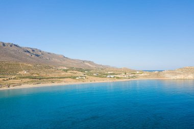 Berrak mavi suyu, yuvarlanan tepeleri ve Girit 'in Ambelou yakınlarındaki bulutsuz gökyüzü altında dağınık evleri olan sakin kumlu bir körfezin geniş manzarası..
