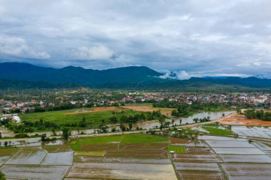Su basmış pirinç tarlaları, ince setlerle ayrılmış su ve yeşil bir yama ile Vang Vieng, Laos 'un kenarına doğru uzanır. Kasaba, bulutlu bir gökyüzünün altında ormanlık dağların eteklerinde oturur ve yağmurlu havada kırsal araziyi yakalar.