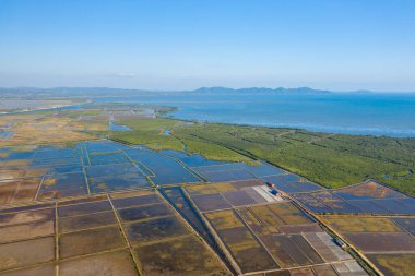 Kamboçya, Kamboçya yakınlarındaki yemyeşil mangrovlarla çevrili geometrik tuz buharlaşma göletlerinin geniş hava manzarası. Manzara yansıtıcı su yüzeyleri, yama alanları ve bulutsuz bir gökyüzünün altındaki uzak tepeleri içerir..