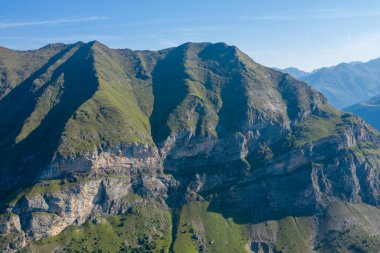 Yeşil yamaçlar ve açık kayalıklar Pireneler 'deki Gavarnie Gedre yakınlarında güneşli bir dağ yamacında dramatik desenler oluşturur. Kıtır sabah ışığı engebeli arazideki dokuları ve derin gölgeleri güçlendirir..