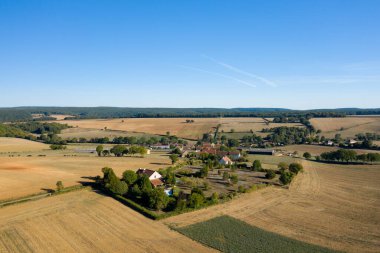 Geniş hava manzarası, geniş altın tarlalar, dağınık ağaçlar ve açık mavi gökyüzünün altındaki uzak ormanlık alanlarla çevrili küçük bir köy olduğunu gösteriyor. Açık tarım arazileri ve nazik tepeler Nievre 'de kırsal bir sakinlik ve ferah bir hava yaratıyor.