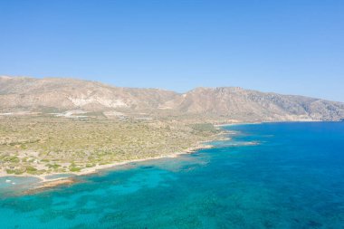 Kristal berraklığında Akdeniz suyu, Girit 'te engebeli ve el değmemiş bitki örtüsü ve kurak dağlarla çevrili bir kıyı şerididir. Parlak güneş ışığı ve derin mavi gökyüzü doğal dokuları ve sakin atmosferi güçlendirir..