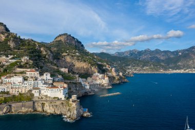 Geniş bir hava perspektifi, İtalya 'nın Amalfi kentindeki beyaz yıkanmış binaları yakalıyor ve engebeli kayalıklardan canlı mavi Akdeniz' e doğru çağlayarak ilerliyor. Dramatik kıyı şeridi teraslı yamaçlar, yemyeşil yemyeşil ve uzak dağlarla çevrili.