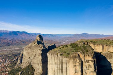 Yunanistan 'ın Meteora kentindeki Thessaly ovasının üzerinde yükselen dikey kumtaşı monolitler berrak mavi gökyüzü ve uzak sonbahar dağları bir uçurum ve sükunet hissi yaratıyor..