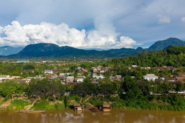 Geleneksel çatıları, yemyeşil yeşilliği ve ön plandaki kahverengi Mekong Nehri ile Luang Prabang 'ın manzarası yükseldi. Orman dağları ve dramatik kümülüs bulutları parlak gün ışığında çarpıcı bir zemin oluşturur..