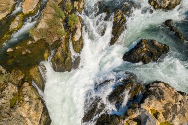 Laos 'un güneyindeki Champasak Eyaleti' ndeki Li Phi Şelalesi olarak da bilinen Tat Somphamit Şelaleleri 'ndeki engebeli kayaların arasından akan girdap gibi beyaz suyun ayrıntılı hava görüntüsü. Sahne, desenli taş, yosunlu yamalar ve enerjik su akışını ön plana çıkarıyor.
