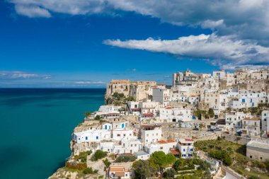 Peschici 'deki durgun turkuaz denize bakan engebeli uçurumların tepesine tünemiş, parlak mavi gökyüzü altında, dağınık bulutlarla bembeyaz binalar yığıldı..