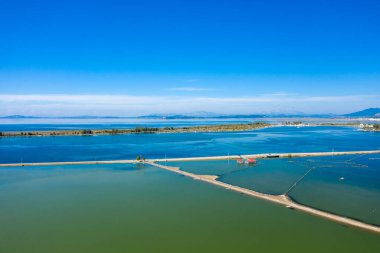 Yunanistan 'ın batısındaki Missolonghi tuz bataklıklarının canlı hava perspektifi, temiz bir gökyüzü altında geometrik setler, mavi ve yeşil sular ve uzak sıradağlar yer alıyor. Huzurlu manzara açık alanı ve doğal desenleri vurgular.
