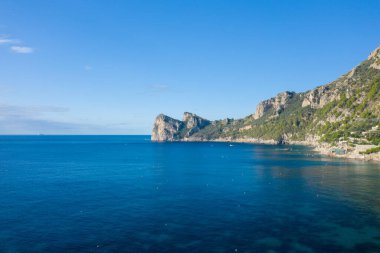 Açık mavi sular, İtalya 'nın kırsal kıyı şeridi boyunca uzanan engebeli kireçtaşı kayalıklarıyla kesişiyor. Güneş ışığı, canlı bir gökyüzünün altındaki yemyeşil ve kayalık kıyı şeridini vurguluyor. Huzurlu bir Akdeniz manzarası hissi uyandırıyor..