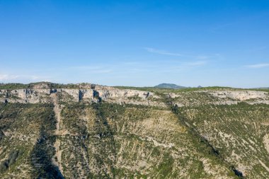 Navacelles Sirki 'ndeki sarp, yeşil noktalı yamaçlı engebeli kireçtaşı sırtı geniş görüş alanına sahip. Açık mavi gökyüzü, açık alan ve doğal ihtişam hissini arttırır..