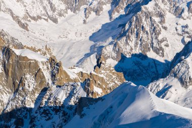 Karla kaplı dramatik yamaçlar ve Mont Blanc kalabalığındaki engebeli granit tepeler, koyu mavi gölgeler ve keskin kış ışığı alp dokularını vurguluyor..