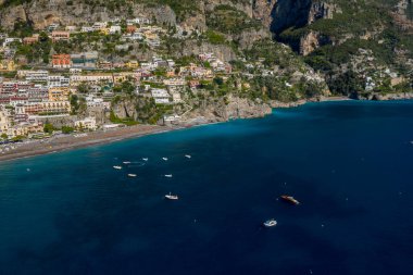 Positano, İtalya 'nın renkli teraslı binaları, canlı mavi Akdeniz' in üzerindeki sarp kayalıklar. Küçük tekneler, bereketli yeşillik ve dramatik kireçtaşı yamaçlarıyla Amalfi Sahili ikonik manzarasını çerçeveleyen kumlu kıyı şeridinde yüzerler..