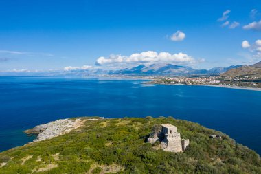Isola di Cirella 'nın hava perspektifi. Etrafı yemyeşil bitki örtüsü, derin mavi Akdeniz suları ve parlak, berrak gökyüzünün altındaki uzak dağlarla çevrili eski taş kalıntıları..