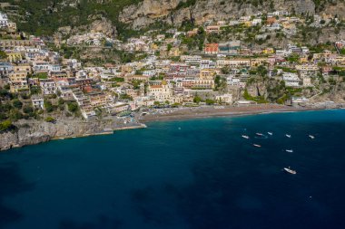 Positano, İtalya 'nın geniş hava perspektifi, sarp kayalıklardan şemsiyelerle kaplı kumlu bir sahile kadar uzanan canlı teraslı evleri gösteriyor. Derin mavi Akdeniz suları küçük teknelerle doluyken yemyeşil ve dramatik kireç taşları yemyeşil.