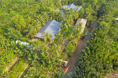 Genel bakış açısı, Hindistan cevizi palmiyeleri ile çevrili teneke çatılı kırsal evleri ve Ben Tre, Mekong Delta, Güney Vietnam yakınlarındaki dar bir kanal boyunca uzanan verimli tropikal bitki örtüsünü yakalar. Sahne canlı yeşillik içeriyor, düzenli olarak.