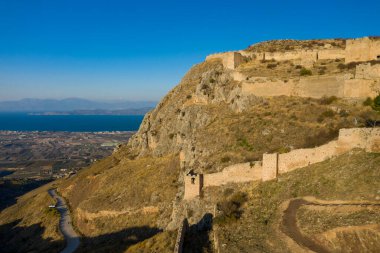 Akrokorint kalesinin tarihi taş duvarları, Yunanistan 'da berrak gökyüzünün altında Korint Körfezi' nin mavi suları ve tarım arazilerine tepeden bakan engebeli yamaçların izini sürüyor..