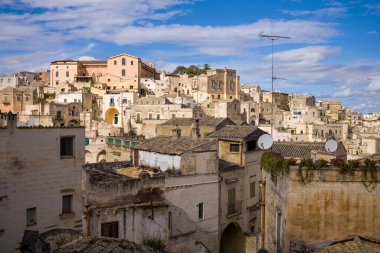 Matera, İtalya 'daki yamaç boyunca yoğun bir tarihi kireçtaşı binası düzeni yükseliyor, bulutlarla kaplı bir gökyüzünün altında. Yıpranmış dokular ve çeşitli çatılar zengin bir Akdeniz kentsel manzarası yaratır.