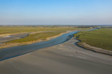 Bereketli bataklıklarla ve açık mavi gökyüzünün altındaki geniş kumlu düzlüklerle çevrili kıvrımlı gelgit nehrinin hava perspektifi. Manzara açık, güneşli ve sakin, yumuşak doğal dokuları var..