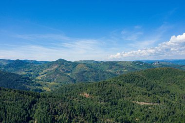 Yoğun ormanlık tepelerin ve Ardeche bölgesinde dağınık çayırların bulunduğu yuvarlanan arazinin hava manzarası canlı mavi gökyüzünün altındaki parlak güneş ışığıyla aydınlatılıyor..