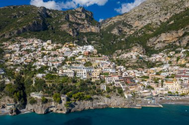 İtalya 'nın Positano kentinin panoramik hava manzarası. Amalfi Sahili' nin turkuaz sularına uzanan sarp kayalıklardan akan renkli teraslı evler. Canlı Akdeniz köyünün arkasında, berrak mavi gökyüzünün altında dramatik kireçtaşı dağları yükseliyor..