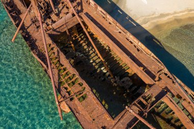 Dimitrios 'un, Yunanistan' ın Gythio kenti yakınlarındaki kumlu bir sahil kenarındaki sığ saydam sulardaki paslı, iskelet gövdesinin hava görüntüsü. Güneş ışığı, aşınmış dokuları ve çürümüş metal yapısını ortaya çıkarır..