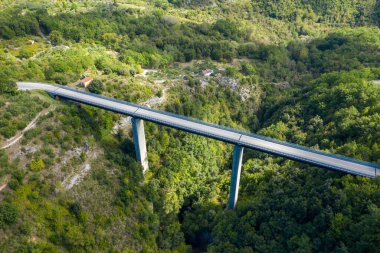 İtalya 'nın Rivello kenti yakınlarındaki derin ve ormanlık bir geçitten geçen parlak bir köprünün havadan görüntüsü. Güneş ışığı, canlı yeşilliği ve dramatik manzarayı vurguluyor. Yapının temiz çizgileriyle çarpıcı bir kontrast oluşturuyor..