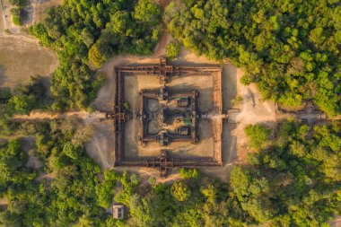 Angkor bölgesinde yoğun tropikal ormanlarla çevrili Banteay Samre tapınağının simetrik kuş bakışı perspektifi. Antik kumtaşı kompleksi, sıcak gün ışığında kırsal açıklıkların ortasında, tarihi mimarisini ve