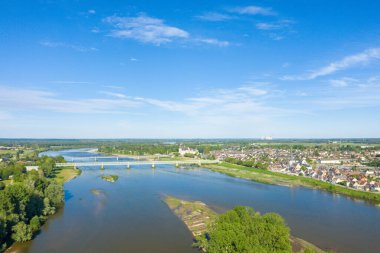 Loire Nehri 'nin köyü geçtiği Sully-sur-Loire' ın geniş hava manzarası, denizi geçen uzun bir köprü ve berrak mavi gökyüzünün altında yemyeşil bir yer. Sahne aydınlık, açık ve huzurlu..
