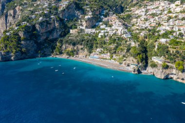 Positano, İtalya 'nın geniş hava perspektifi sakin bir kumlu sahil ve canlı mavi Akdeniz sularının üzerindeki teraslı yamaçlı evleri ortaya çıkarıyor. Kıyıya yakın yüzen küçük tekneler, dramatik uçurumlar ve bereketli yeşilliklerle kıyı sahnesini çerçeveliyor..