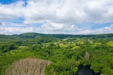 Dağınık evleri, geniş yeşil tarlaları ve Morvan bölgesinde parçalı bulutlu bir gökyüzü altında yoğun orman tepeleri olan yemyeşil bir kırsal alan..
