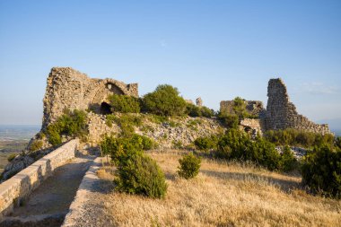Chateau de Opoul Perillos 'un antik taş kalıntıları altın çimenlerin ve vahşi çalıların üzerinde yükselir, açık mavi gökyüzüne karşı sıcak akşam güneşinde yıkanır..