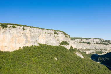 Gorges de Ardeche 'deki sık ağaçlı bir vadinin üzerinde yükselen kireçtaşı kayalıkları parlak güneş ışığı altında parlak mavi bir gökyüzü altında yıkandı. Engebeli kayalar, aşağıdaki zengin yeşilliklerle tezat oluşturuyor..