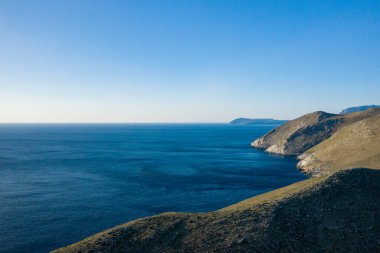 Kayalık tepelerin, Yunanistan 'ın Cap Tenare kentindeki sakin, derin mavi Akdeniz' le buluşmasını gösteren geniş bir manzara. Berrak gökyüzü ve güneş ışığı engebeli dokuları ve engin açık suları vurguluyor. Huzur ve mekanı çağrıştırıyor..