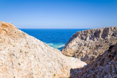Beyazlatılmış kayalık kayalıklar Girit 'teki Seitan Limania' da küçük kumlu bir sahile ve canlı mavi sulara uzanan dramatik bir vadi oluşturur. Açık gökyüzü ve engebeli dokular çarpıcı bir Akdeniz manzarası yaratır..