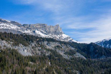 Tete 'nin kireçtaşı kayalıkları yoğun bir kozalaklı ormanın üzerinde yükseliyor. Kar parçaları ve parlak mavi bir gökyüzü, canlı bir alp manzarası yaratıyor..