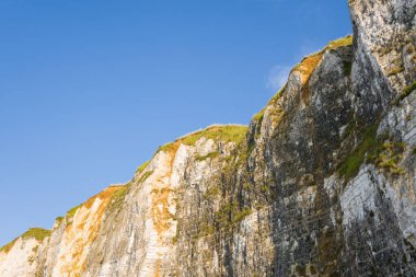 Parlak güneş ışığı, Normandiya 'da açık mavi gökyüzüne yeşil çimlerle kaplı engebeli beyaz tebeşir uçurumlarını aydınlatarak doğal dokuları ve dramatik dikey çizgileri vurguluyor..