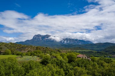 Geniş yeşil vadi ağaçlarla ve dramatik dağ zirvelerinin altında kısmen bulutlarla örtülü kırsal çiftlik evleriyle dolu. Parlak gün ışığı ve canlı renkler yeni ve davetkar bir kırsal manzara yaratır..