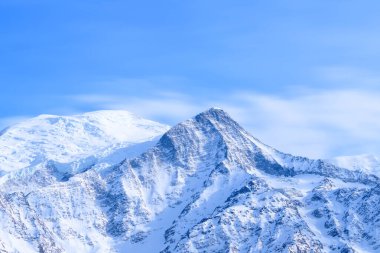 Mont Blanc, kar kaplı yamaçları ve parlak mavi gökyüzünün altında keskin tepeleri ile dimdik ayakta duruyor. Kış dokularını ve sakin alp atmosferini sergiliyor..