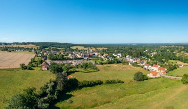 Saint-Honore-les-Bains 'in geniş insansız hava aracı panoraması büyüleyici bir kırsal köy, açık yeşil tarlalar, altın tarlalar ve açık mavi gökyüzünün altındaki ormanı kapsıyor..
