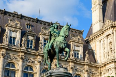 Bronz binicilik heykeli, heykeltraş figürleri ve klasik pencere çerçeveleriyle süslü bir taş binanın önüne kurulmuş. Paris şehir merkezindeki sıcak öğleden sonra ışığıyla aydınlatılıyor..
